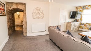 A cozy living room with a sofa, a television, a decorative mirror, and a chandelier. - Castle Keep at Stanhope Castle (Bishop Auckland)
