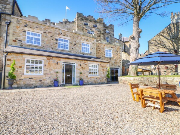 A stone building with a gravel courtyard, a wooden bench, and an umbrella. - Castle Keep at Stanhope Castle (Bishop Auckland)