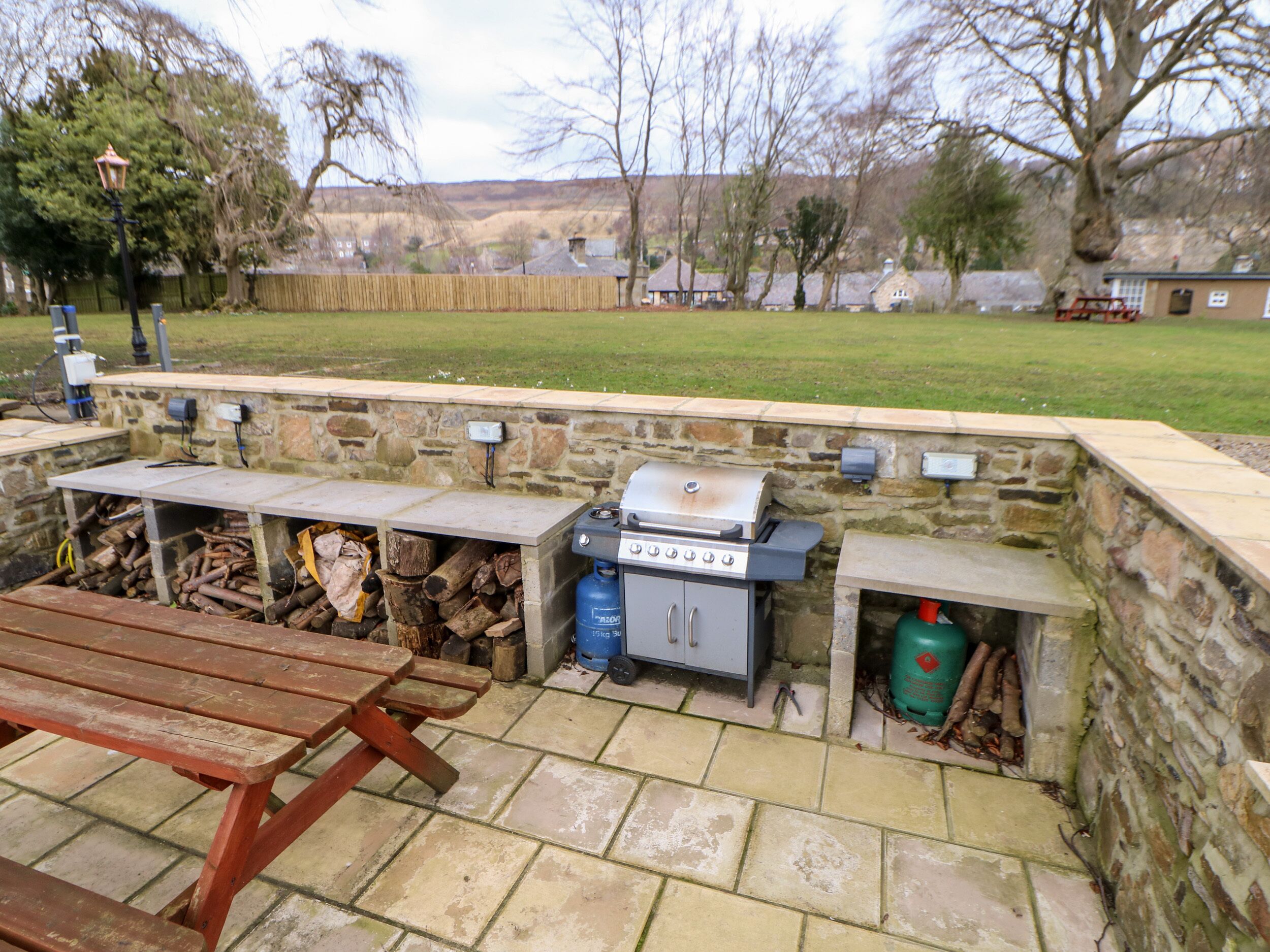 An outdoor barbecue area with stone walls, a grill, and a picnic table.