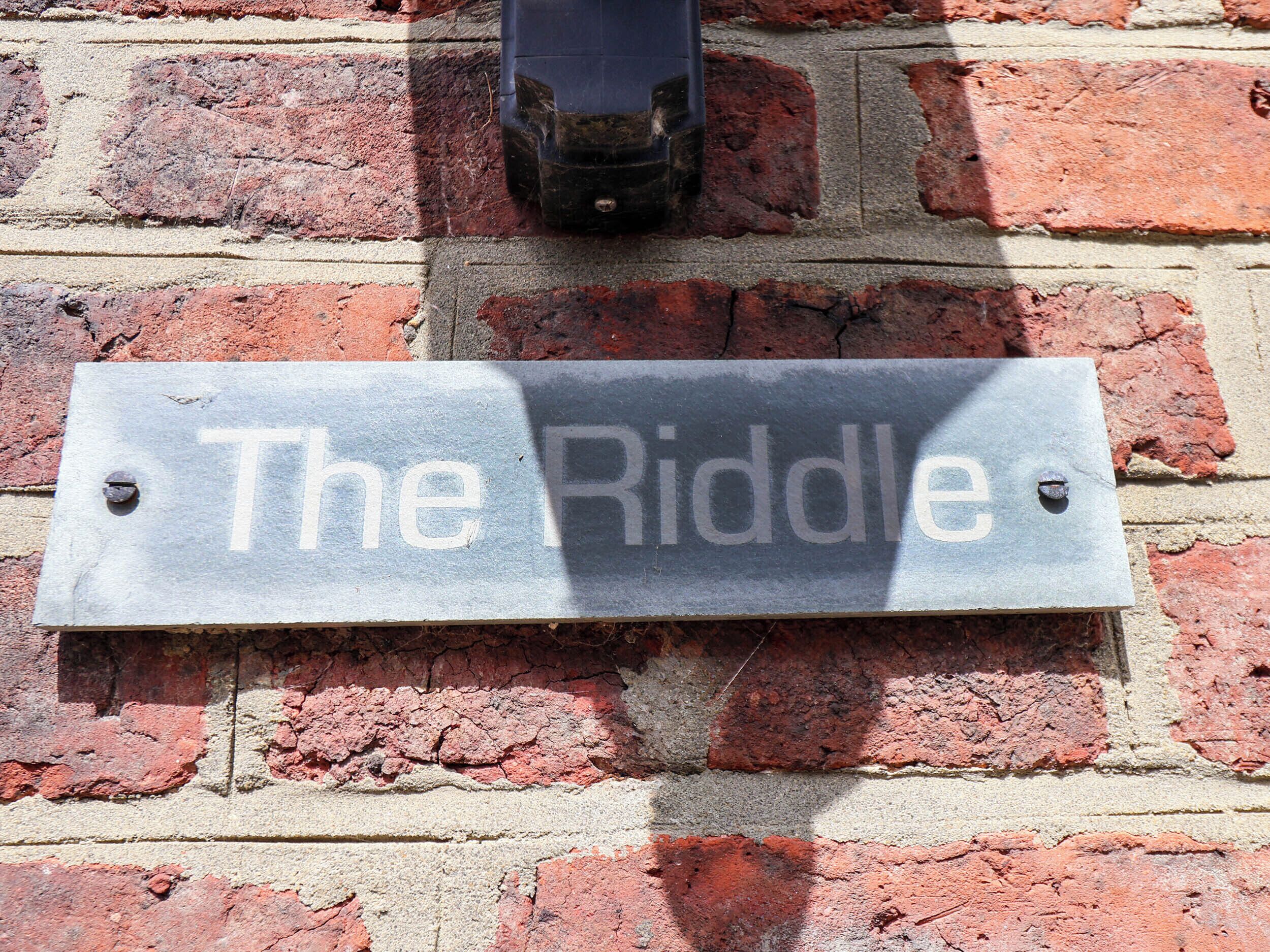 Ein Schild an einer Backsteinmauer mit der Aufschrift 'The Riddle'.