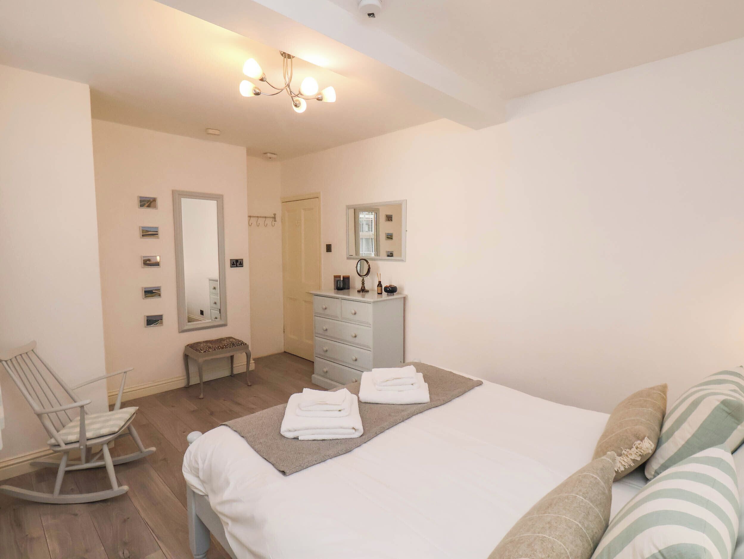 Une chambre à coucher comprenant un lit, une commode, une chaise, un miroir et un luminaire fixé au plafond.