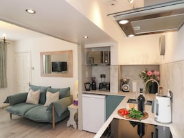 Espaço compacto com cozinha compacta, sofá, mini-frigorífico e área de refeições com chaleira e balança.