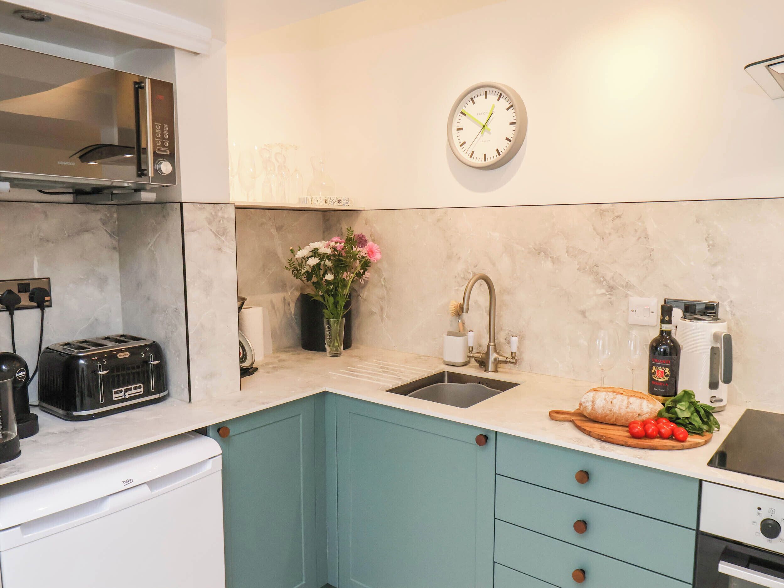 A modern kitchen with a built-in microwave, toaster, sink, and a clock on the wall.
