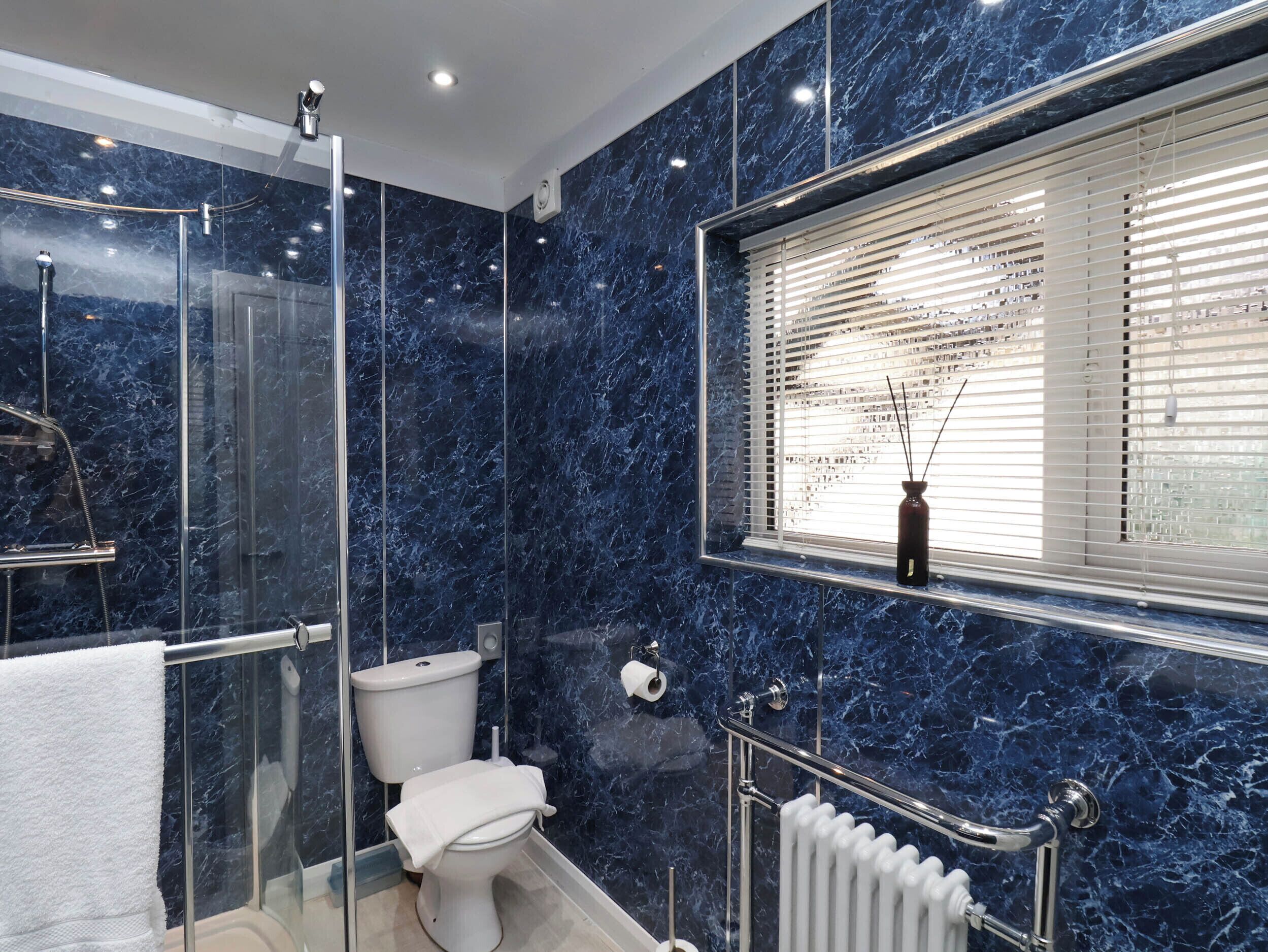 A bathroom with a glass-enclosed shower, a toilet, and a window with blinds.