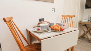 Ruokapöytä, jonka ympärillä on kaksi puista tuolia, pöydällä on lautasilla croissantteja ja vadelmia, ja seinällä on kehystetty kuva.