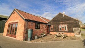 Two brick buildings with red-tiled roofs, a green trash bin, and a wooden picnic table.