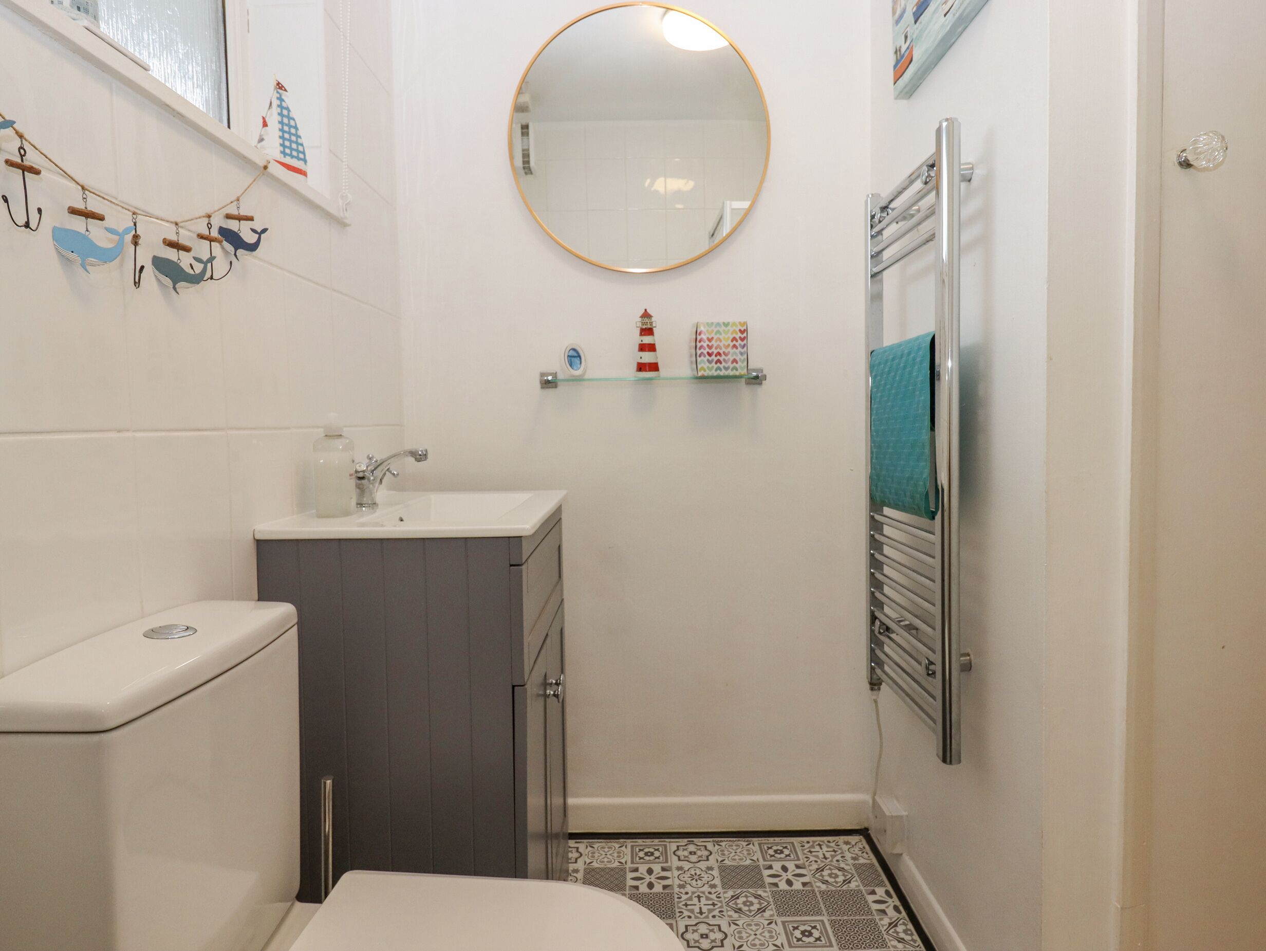 Un baño pequeño con inodoro, lavamanos y espejo. Hay adornos en la pared y un perchero para toallas.