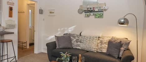 A cozy living room with a grey sofa, a wooden coffee table with a bottle of champagne and glasses, and a small side table.