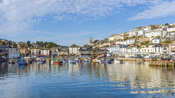 A harbor with boats, a church, and buildings on a hillside. - 3 Dolphin Court (Brixham)