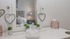 A bedroom with a large mirror, heart-shaped decorations, a bedside table with a lamp, a floral box, and a decorative glass container. - 3 Dolphin Court (Brixham)