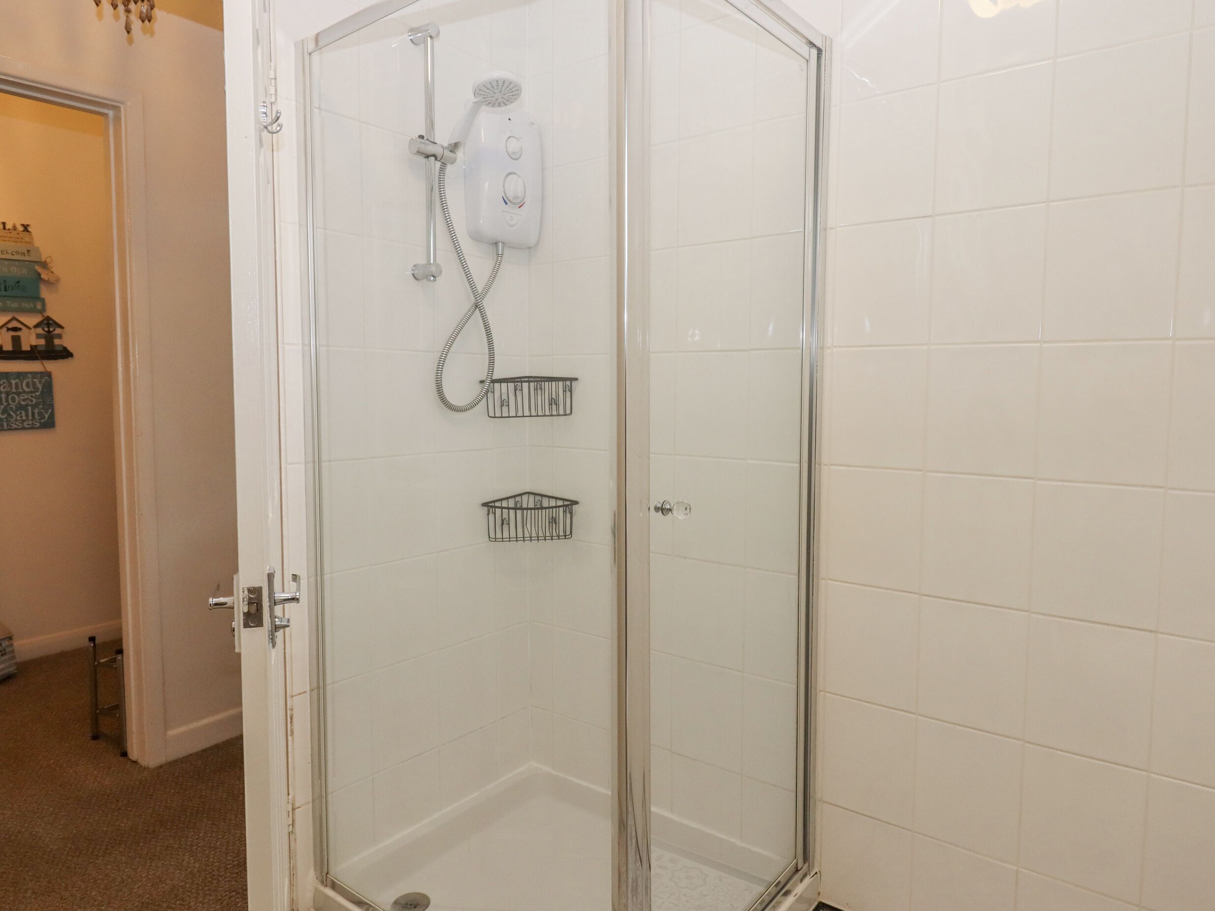 Una ducha con cerramiento de vidrio, cabezal de ducha manual y llave empotrada en la pared.