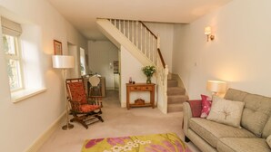 A living room with a sofa, a chair, a rug, a staircase, and a dining area in the background. - Spens Farm Cottage (Lancaster)