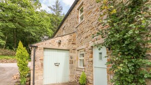 A stone building with a light green door and windows, surrounded by greenery and potted plants. - Spens Farm Cottage (Lancaster)