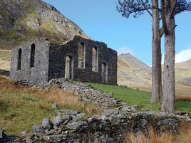 An ancient stone structure with multiple arches, surrounded by a grassy field and a mountain backdrop.