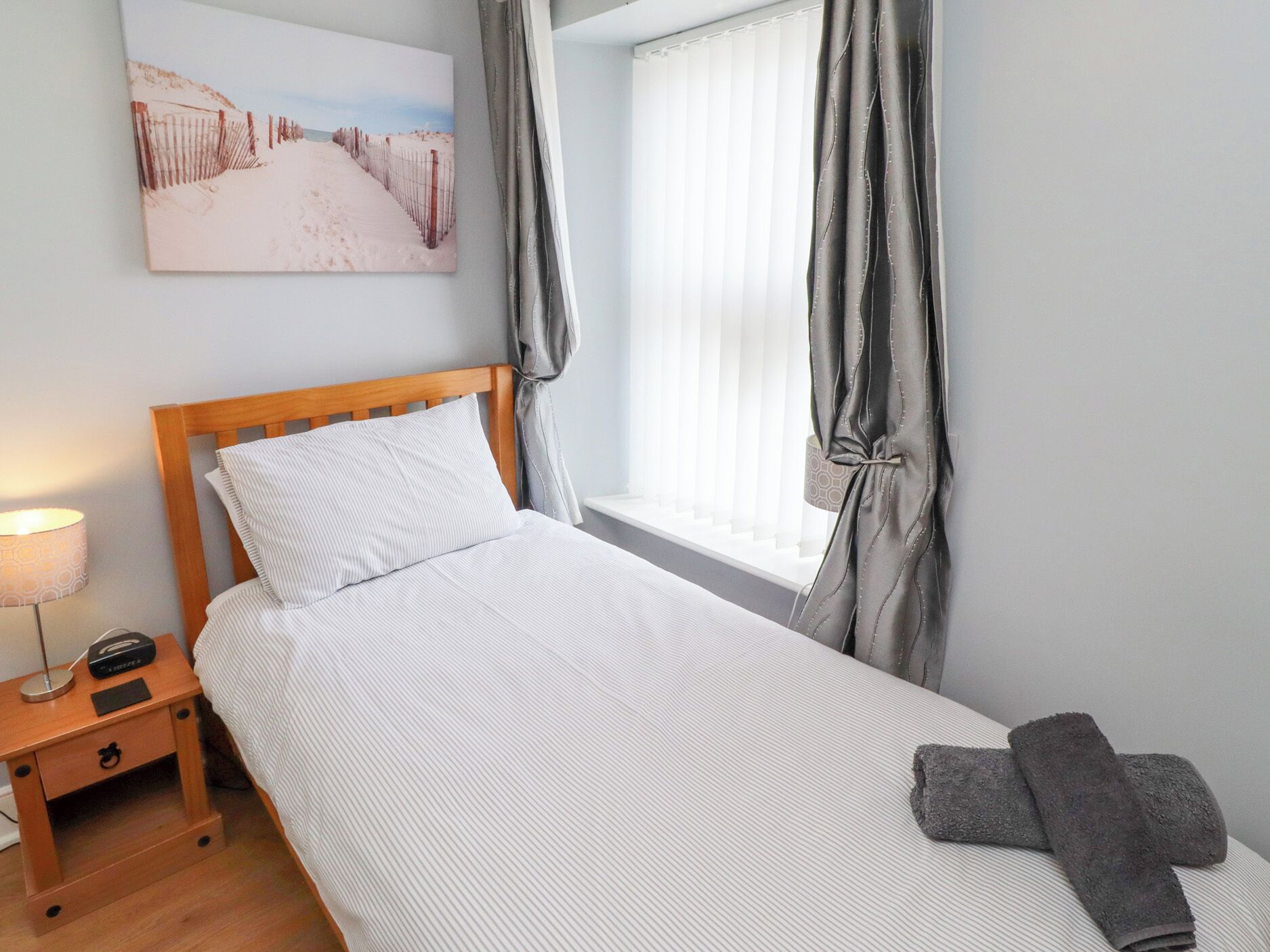 A neatly made bed with a wooden headboard, a bedside table with a lamp, and a window with curtains.