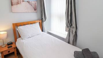A neatly made bed with a wooden headboard, a bedside table with a lamp, and a window with curtains.