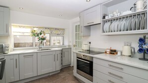 A modern kitchen with white cabinets, a built-in oven, and a countertop with a coffee maker. - Rose Cottage (Lydney)