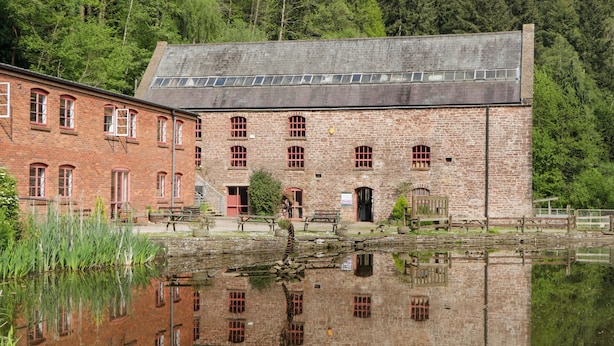 A historic brick building with arched windows and a pond in front. - Rose Cottage (Lydney)