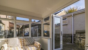 A sunlit room with a sofa, a coffee table with magazines, and a view of the outside. - Rose Cottage (Lydney)