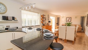 Une cuisine moderne avec un plan de travail noir, des tabourets de bar et un coin repas comprenant une table et des chaises.