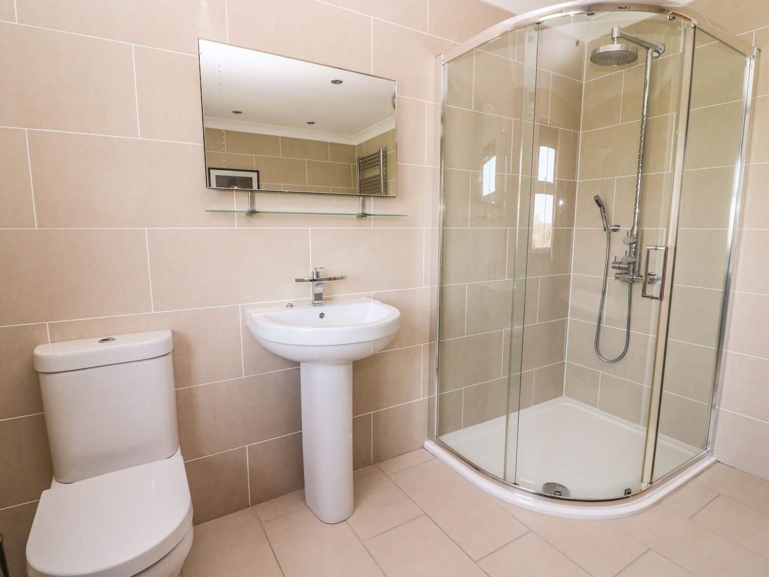 A modern bathroom with a toilet, pedestal sink, and a glass-enclosed shower.