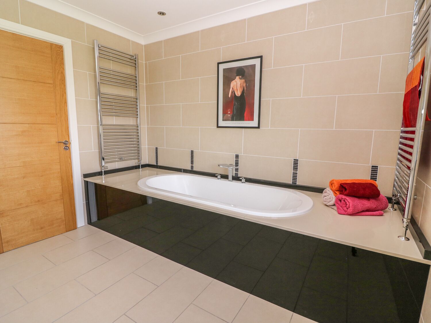 A modern bathroom with a large bathtub, a wooden door, and a towel rack with towels.