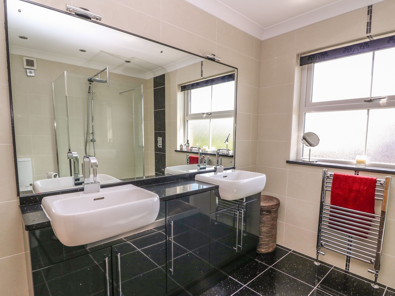 Une salle de bain moderne avec deux lavabos, un grand miroir et une douche.