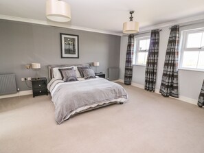 A bedroom with a bed, bedside tables, a radiator, a window with curtains, and a picture on the wall.
