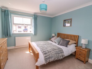 A bedroom with a wooden bed, a nightstand, a dresser, a window with curtains, and a radiator.