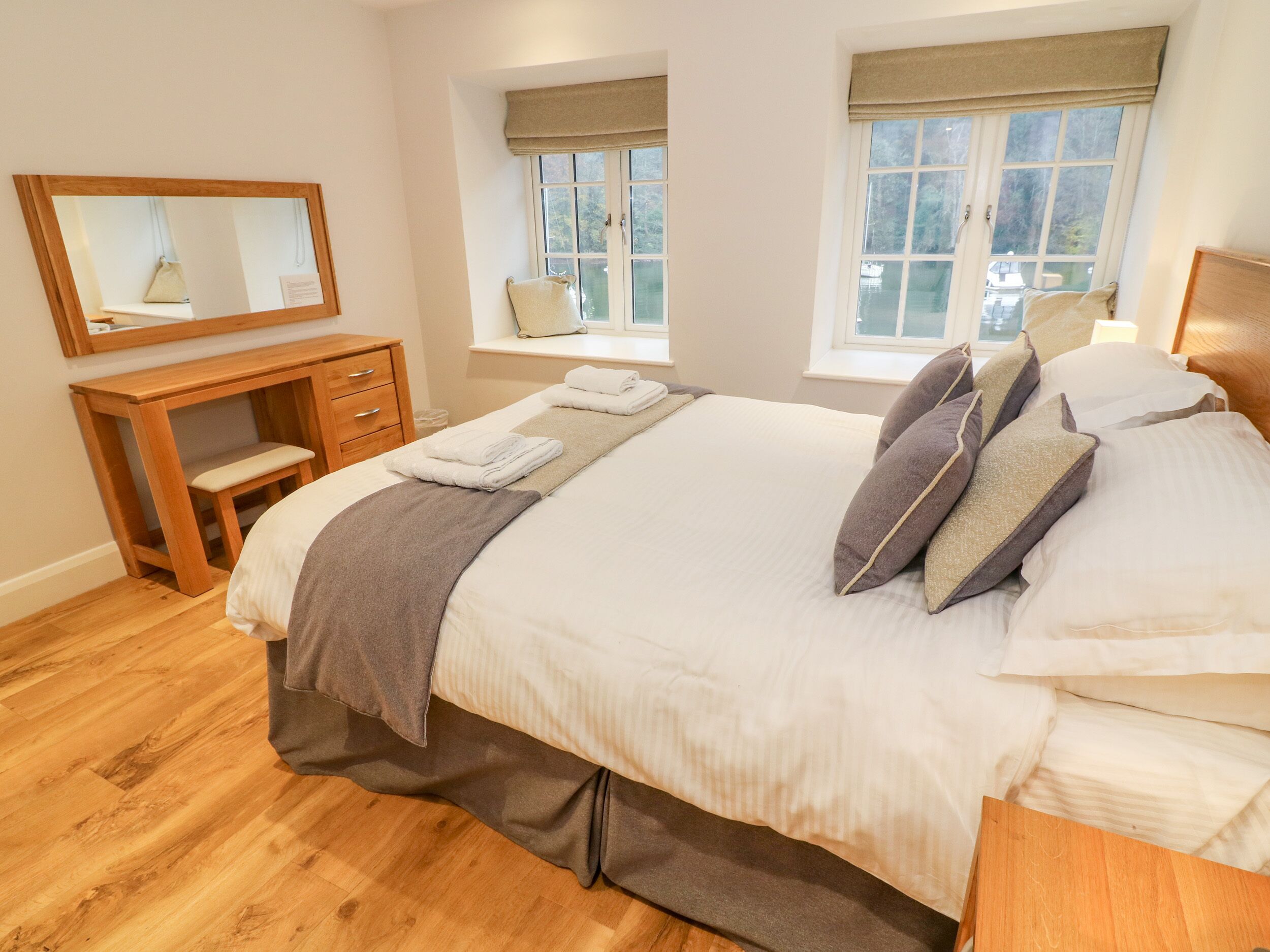 A neatly arranged bedroom with a bed, bedside tables, a desk, and windows with curtains.