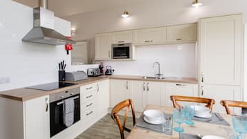 A modern kitchen with white cabinets, a built-in oven, a microwave, and a stainless steel range hood.