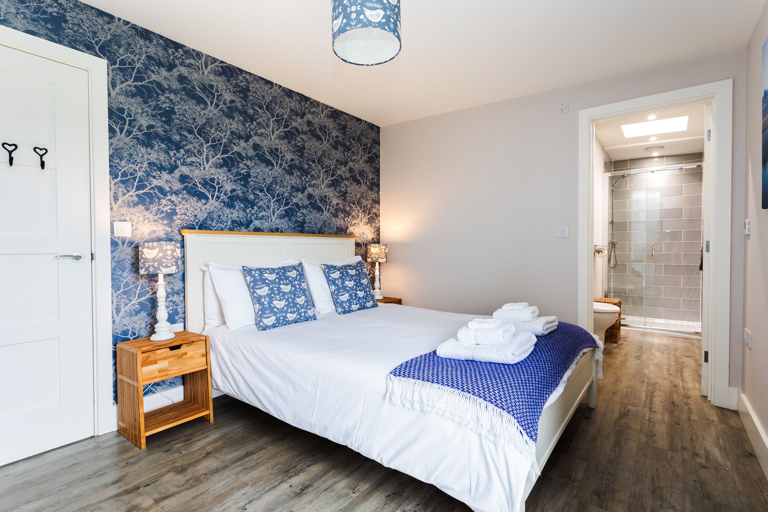 A bedroom with a large bed, a nightstand, a wall-mounted lamp, and a door with heart-shaped hooks.