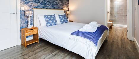 Een slaapkamer met een groot bed, een nachtkastje, een wandlamp en een deur met hartvormige haken.