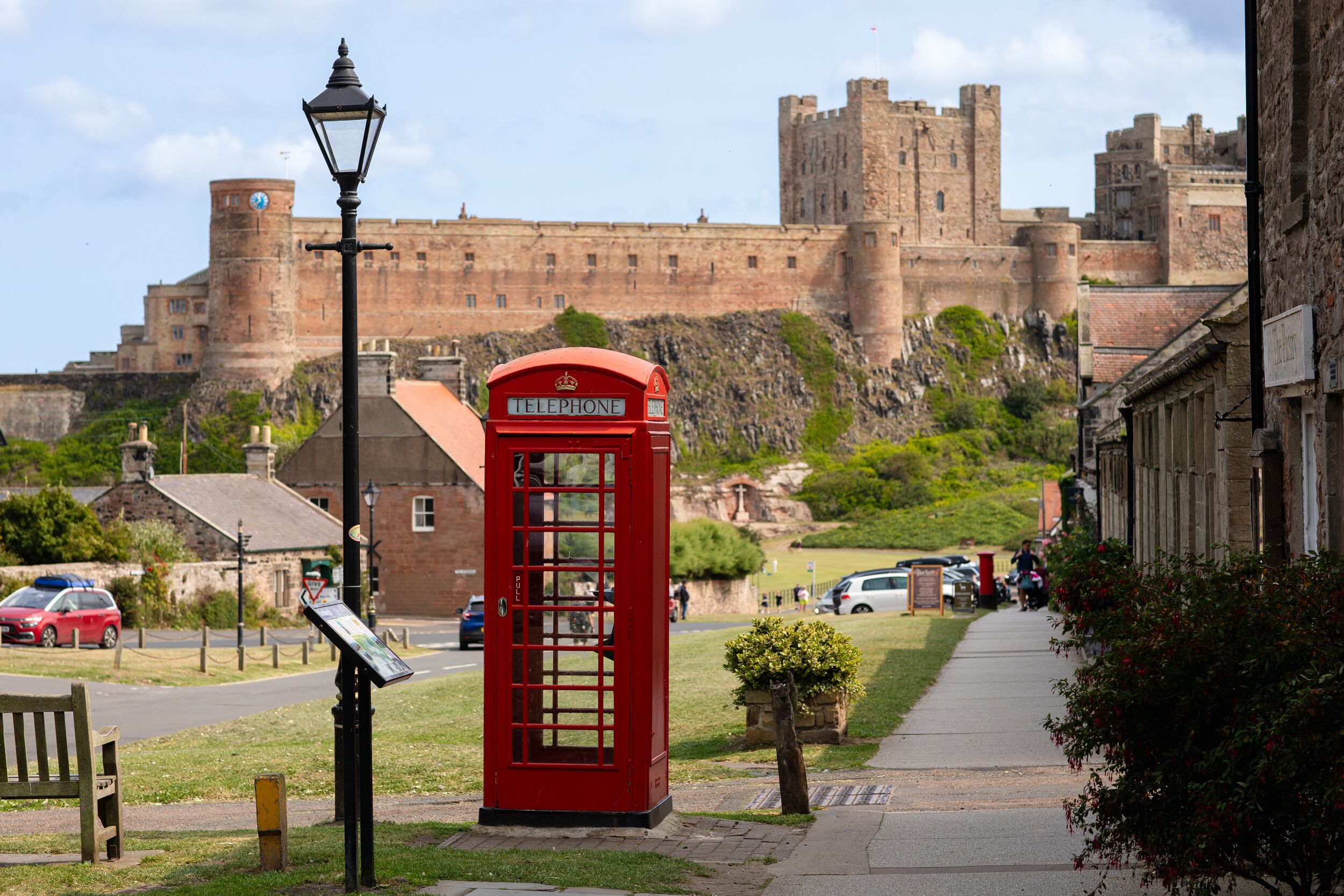 A red telephone booth in a town square with a castle in the background.
