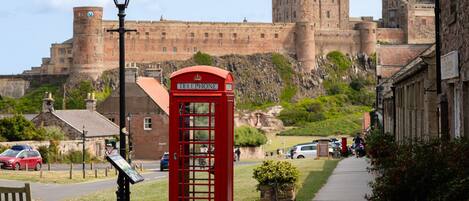 A red telephone booth in a town square with a castle in the background.
