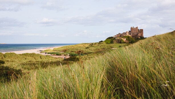 Un paisaje costero con un castillo en una colina cubierta de hierba, con vistas a la playa.