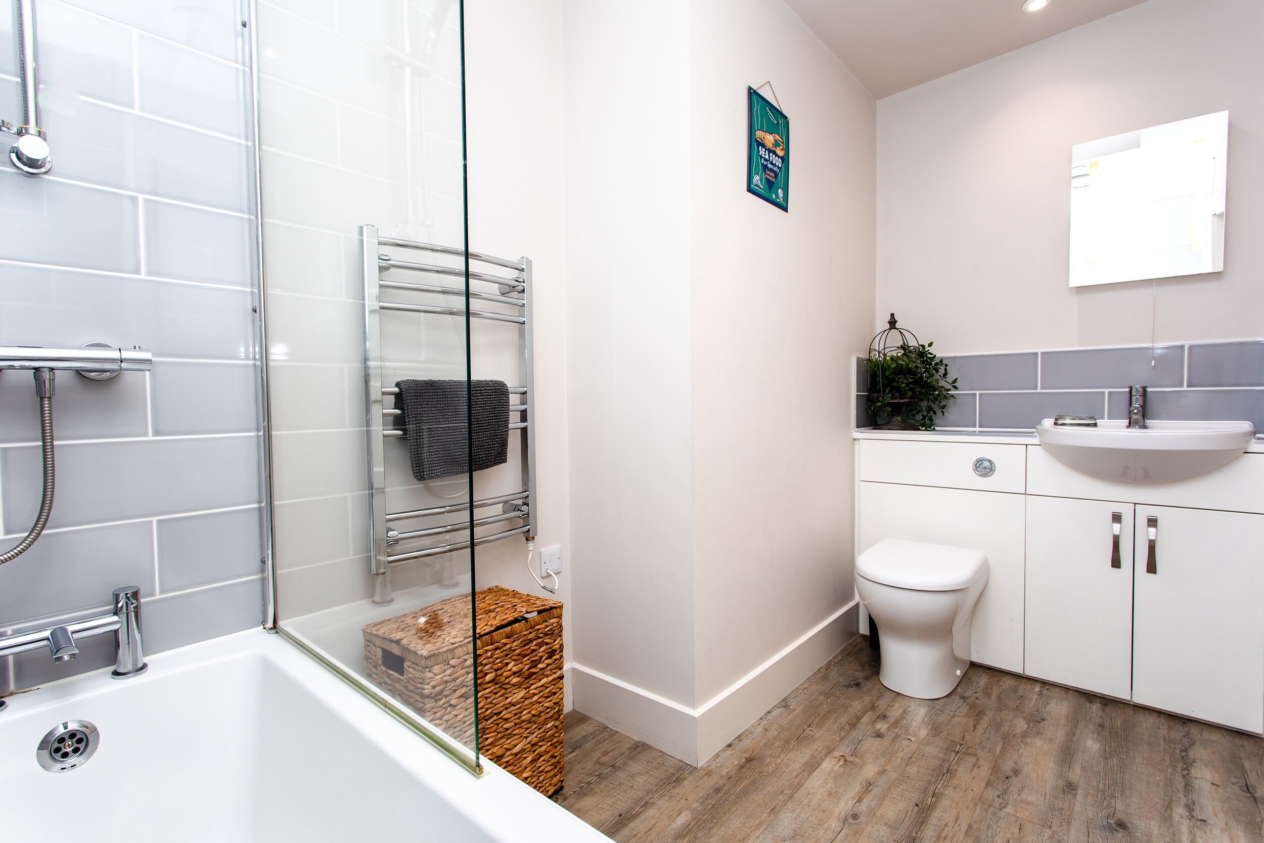 A modern bathroom with a glass shower enclosure, a white bathtub, a white toilet, and a sink with a mirror above it.