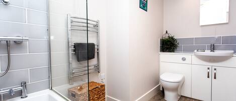 A modern bathroom with a glass shower enclosure, a white bathtub, a white toilet, and a sink with a mirror above it.