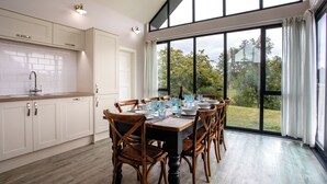 Una cocina moderna con armarios blancos, una mesa grande para seis personas y vista a un paisaje verde a través de amplios ventanales.