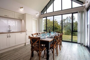 Una cocina moderna con armarios blancos, una mesa grande para seis personas y vista a un paisaje verde a través de amplios ventanales.
