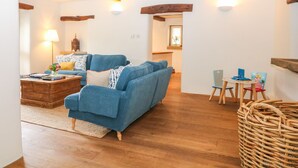A cozy living room with a blue sofa, wooden flooring, and exposed beams. - River Cottage Hayfield (High Peak)