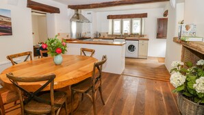 A spacious kitchen with wooden beams, a central island, and a dining area with a round table and chairs. - River Cottage Hayfield (High Peak)