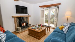 A living room with a fireplace, blue sofas, a coffee table, and a TV mounted on the wall. - River Cottage Hayfield (High Peak)