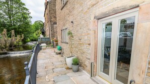 A stone building with a paved patio, a small water feature, and potted plants. - River Cottage Hayfield (High Peak)