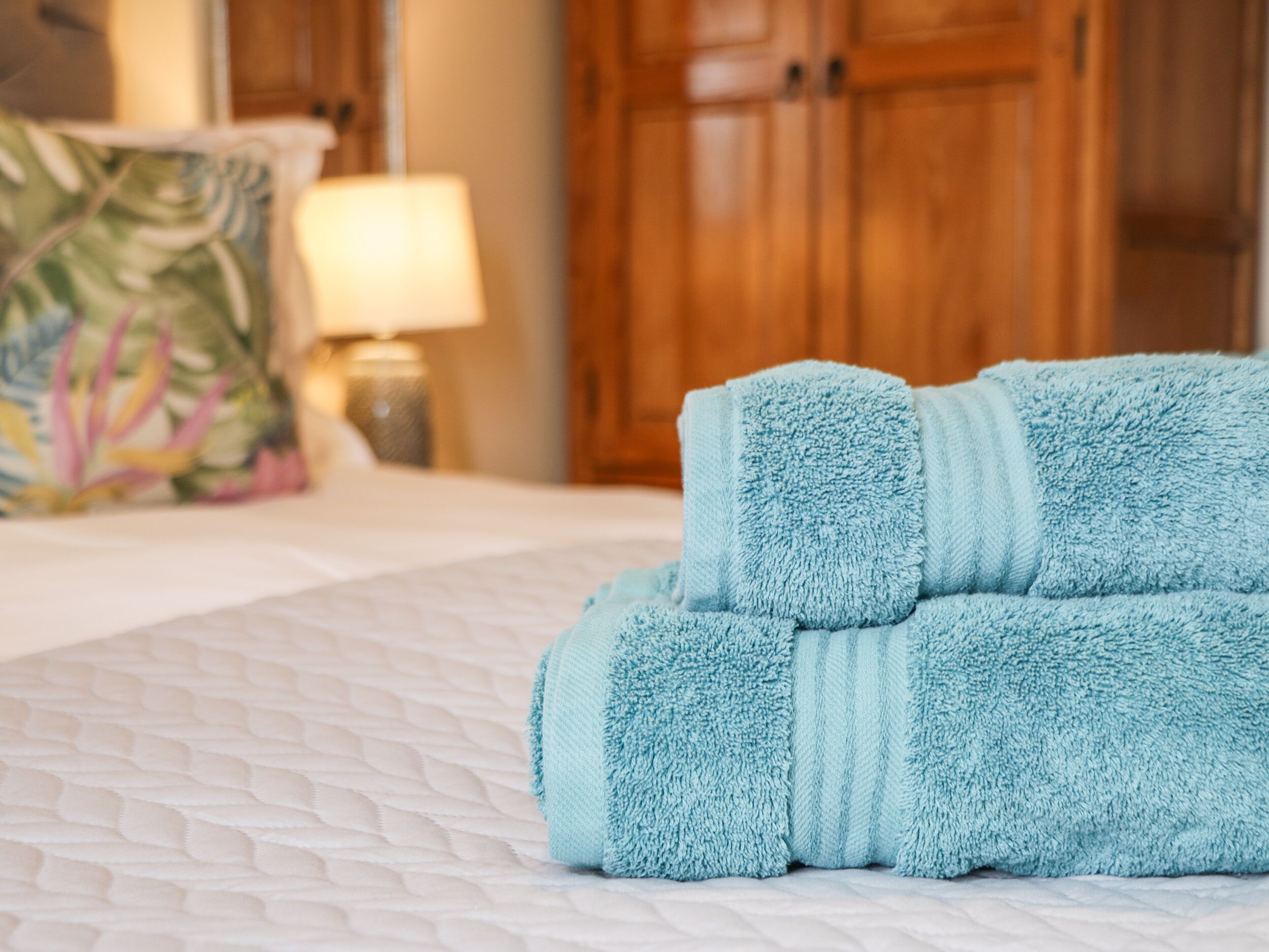 A neatly made bed with a white quilt and two folded towels on it.