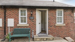 A brick cottage with a green bench outside, a door leading inside, and a sign reading "Crossing Cottage." - Crossing Cottage (Whitby)