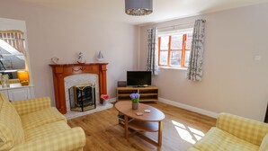 Una sala de estar con chimenea, dos sofás a cuadros, un televisor y una mesa con flores.