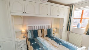 Un dormitorio con cama, dos mesitas de noche, un tocador, una ventana con cortinas y armarios empotrados.
