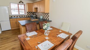 Una cocina compacta con armarios de madera, encimera negra y comedor con mesa de madera dispuesta para dos personas.