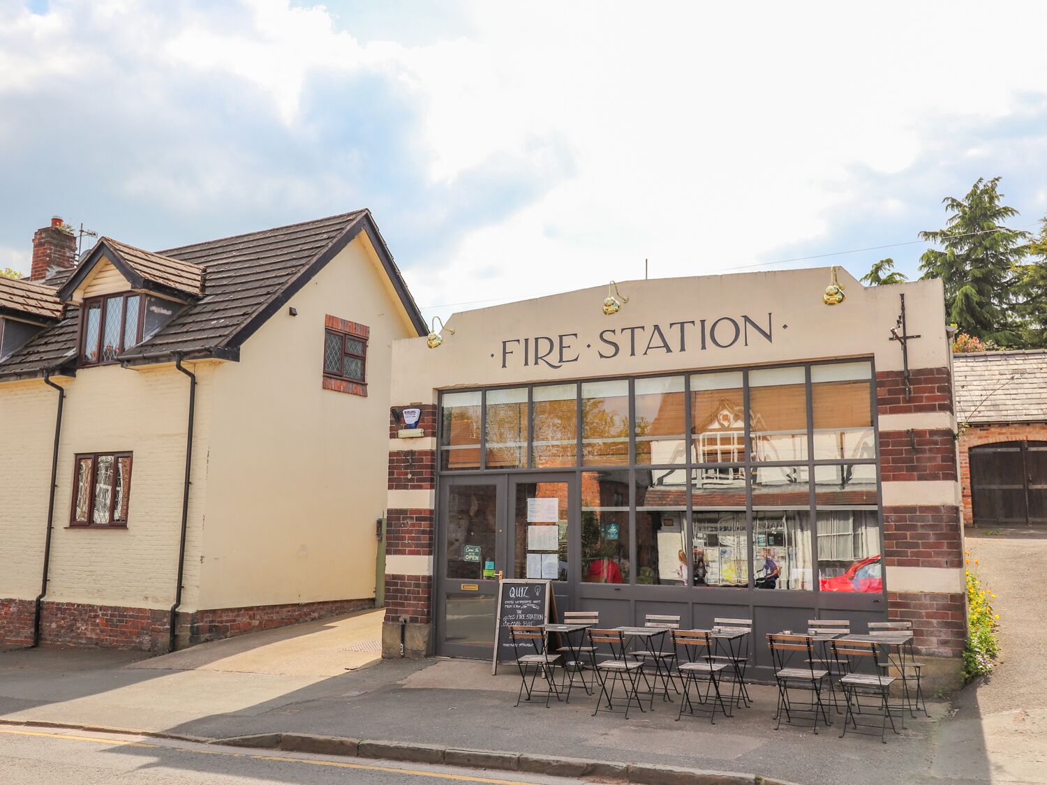 A building labeled "Fire Station" with a large window, outdoor seating area, and a brick facade.